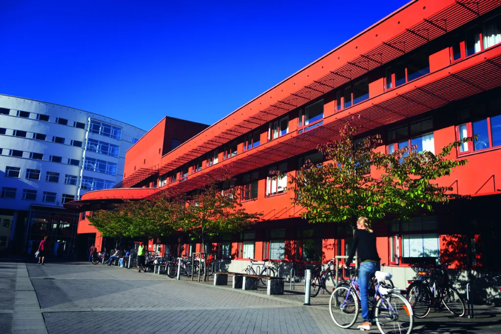 Červená budova Jönköping University s bicyklami pred vchodom a študentkou s bicyklom