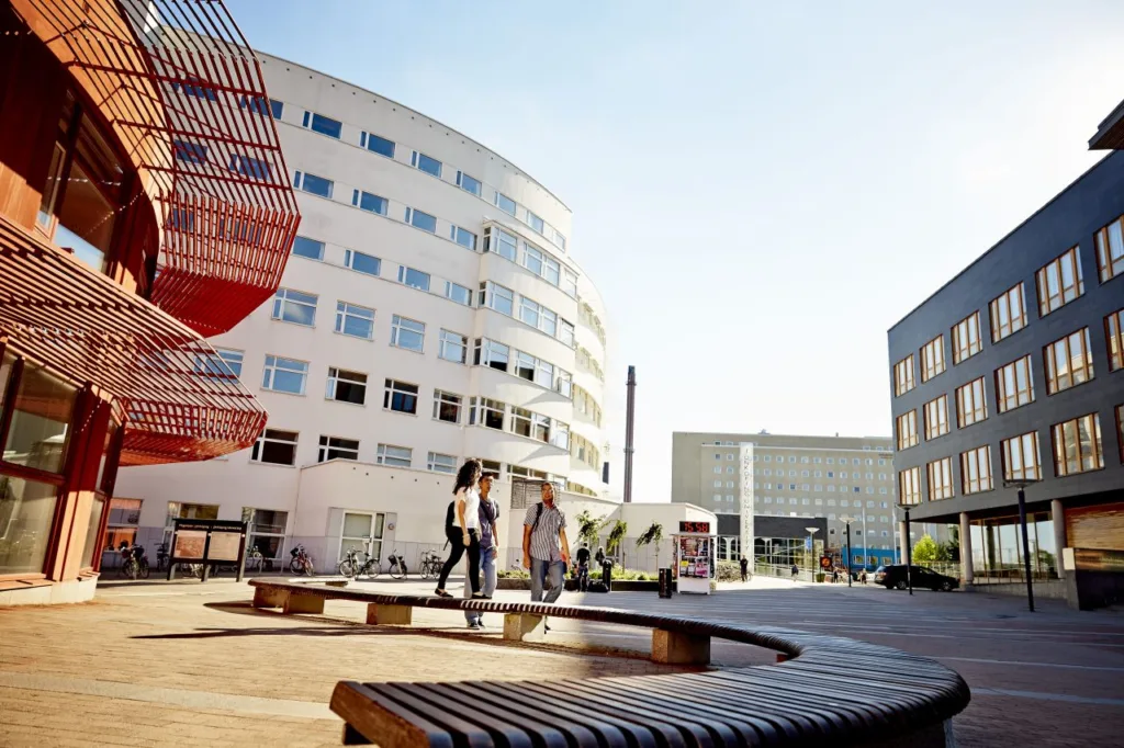 Námestie kampusu Jönköping University s oblúkovou bielou budovou a drevenými lavičkami
