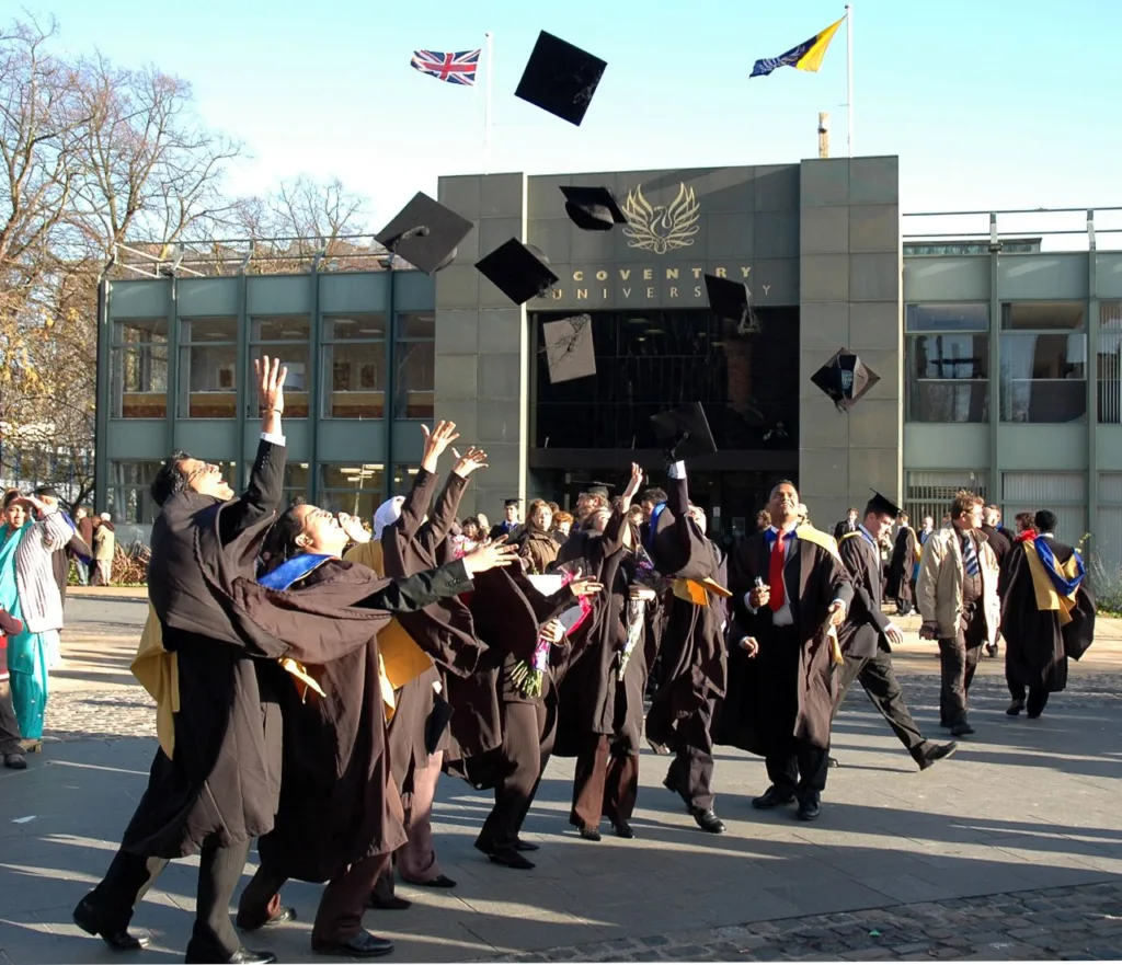 Absolventi Coventry University vyhadzujú klobúky pred budovou univerzity