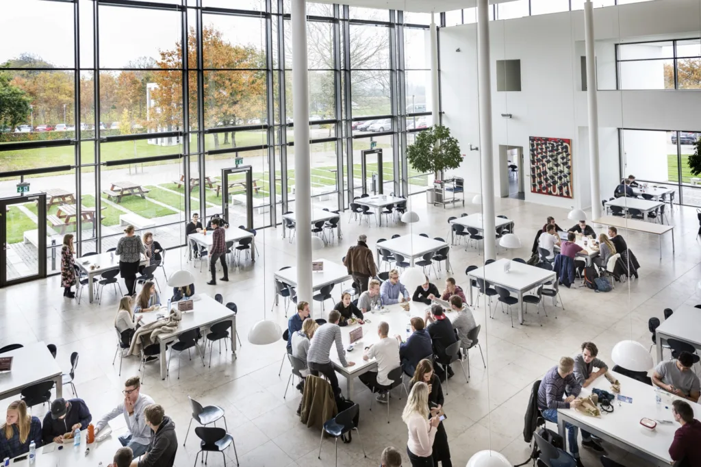 Študenti pri stoloch v presklenej jedálni kampusu Aarhus University v Herningu