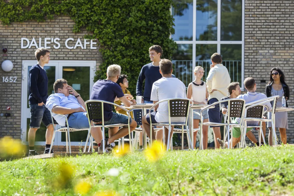 Študenti sedia pri stolíkoch pred kaviarňou Dale’s Café na kampuse Aarhus University