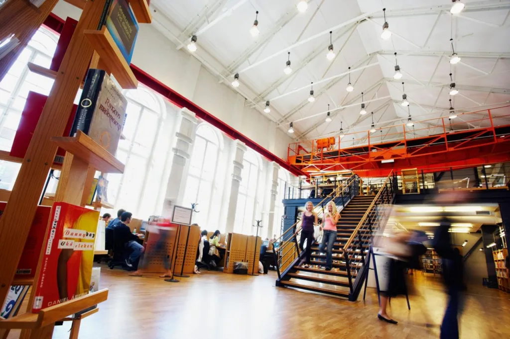 Knižnica Jönköping University s vysokým stropom, schodiskom a študentmi pri stoloch
