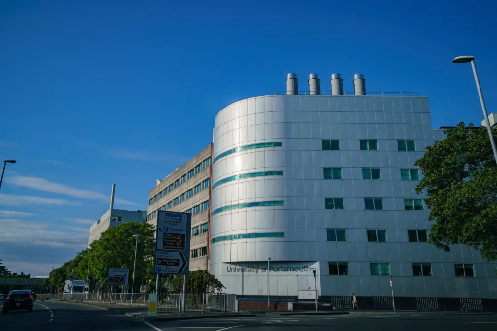 Biela oblá budova University of Portsmouth s nápisom na fasáde pri ceste